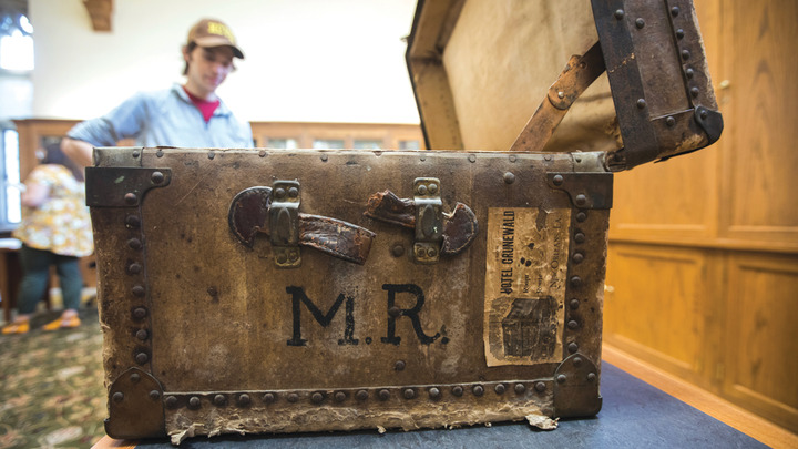 An open 19th century trunk with the initials M.R. on the side with a student standing in the background